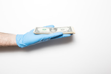 The collapse of the economy due to the coronavirus. Male hand on a white background in medical gloves holds dollars.