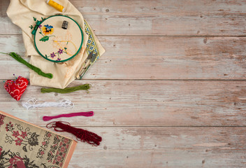 Free time. I like to embroider. Unfinished embroidery in embroidery frames, multi-colored yarn floss, pins, scissors and patterns for embroidery on a light wooden background. Free space.