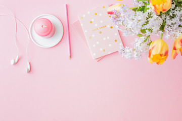 Flat lay blogger or freelancer workspace with a notebook and yellow tulips branches of lilac on a pink background