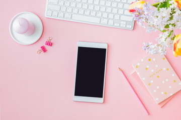 Flat lay blogger or freelancer workspace with a  keyboard, yellow tulips and branches of lilac, office supplies on a light background