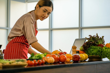 THe young pretty Asian housewife searching  notebook for recipe  of  the meal cook in the kitchen during COVID-19 virus quarantine at home