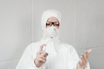 selective focus of person in white hazmat suit, respirator and goggles disinfecting hands with hand sanitizer, coronavirus concept