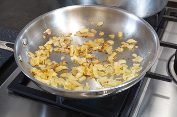 Onion pieces frying in a frying pan on the gas cooker