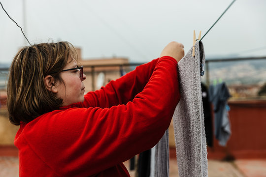 una mujer, ama de casa, cuelga la ropa con pinzas de tender en un cable del tendedero en el tejado de un piso, esta nublado. trabajos dom&eacute;sticos, tareas del hogar.