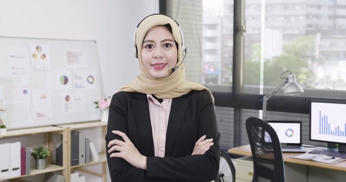 slow motion successful arabic female support phone operator in headset standing in workplace office in company. young woman with headphone wearing black suit smiling face camera with confident.