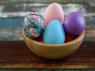 Easter egg, multicolored in a wooden bowl, on a wooden table top.