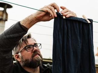 un hombre cauc&aacute;sico con barba en chandal tiende la ropa en el tejado de un edificio. De estilo de vida hipster .