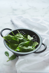 Young fresh leaves of spinach in a black colander.