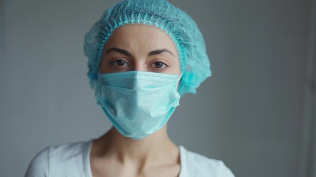 Portrait of a female doctor or nurse wearing medical cap and face mask looking at the camera on grey background. Ready to receive patients in hospital. Health care, medical concept.