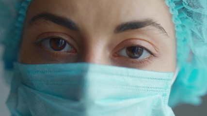 extreme closeup face and eyes woman doctor or nurse wearing medical cap and face mask looking at the camera. Ready to receive patients in hospital. Health care, medical concept. - Powered by Adobe