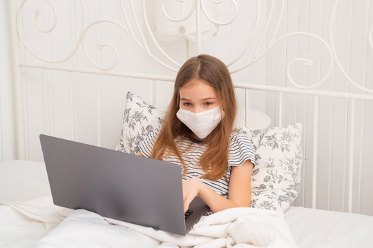 girl in medical mask in bed studying on laptop.