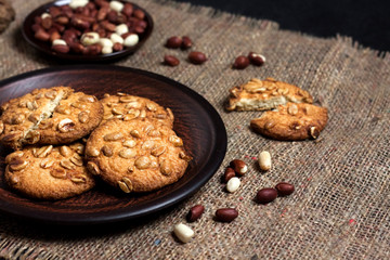 Homemade peanut cookies on a brown plate with raw peanuts in background