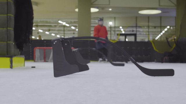 Zoom out of two hockey players training on ice rink using special hockey equipment