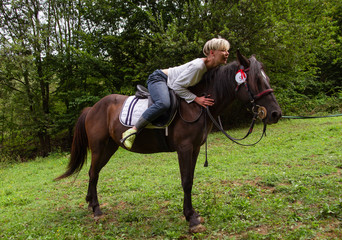 woman hugs a horse by the neck, sitting astride