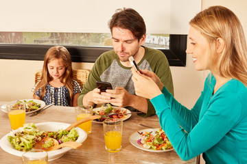 Eltern und Tochter mit Smartphone beim Mittagessen
