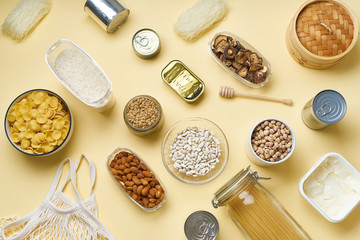 Creative flatlay with pantry staples. Glass jars with pasta, beans and chickpeas, canned goods,...