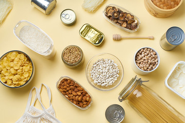 Creative flatlay with pantry staples. Glass jars with pasta, beans and chickpeas, canned goods,...