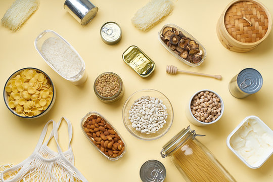 Creative flatlay with pantry staples. Glass jars with pasta, beans and chickpeas, canned goods, nuts and dried mushrooms in reusable containers. Top view pattern with basic products
