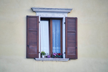 Italian window on the yellow color wall facade with open wooden brown shutters