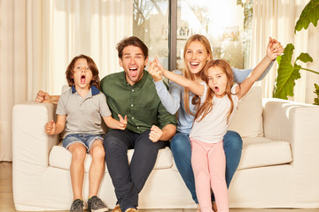 Jubelnde Familie mit zwei Kindern auf dem Sofa