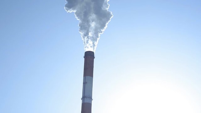 chimneys of a plant closeup. Pipes with thick smoke against a blue sky. Smoke-emitting chimneys.