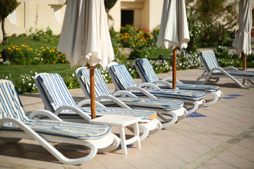 Row of empty swimming pool sun loungers / sun beds with striped matrasses