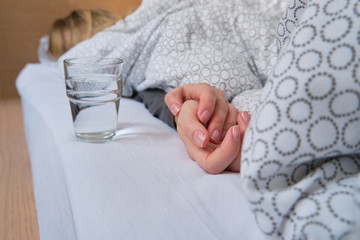 A glass of water next to a girl sleeping in bed. Happy morning. Woman in pajamas. Healthy lifestyle, wellness. Proper nutrition. Drinking water. Morning with water. Sunlight on linens. Pillow, blanket