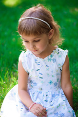 Portrait of a smiling little girl sitting on green grass.