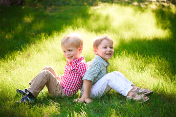 Naklejka na ściany i meble Two brothers are sitting on sunny glade in park