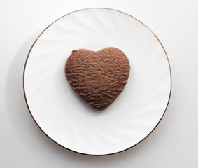 Chocolate cookies in the shape of a heart lies on a white plate with a gold rim. Cake