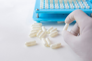White pill capsules in hand wearing white medical gloves on white background