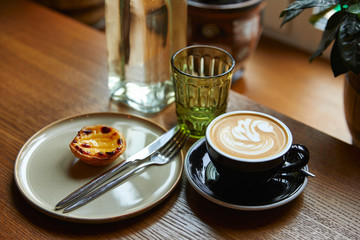 cup of coffee with foam and cake on a plate with cutlery