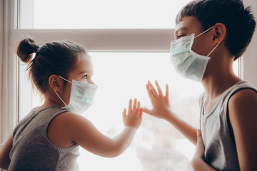 Cute children boy and girl in medical mask is sitting at home in quarantine. Сhildren fun play...