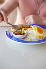 tourist man eating on the beach a Thai dish of rice, eggs and seafood