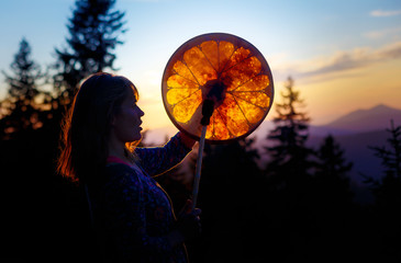 beautiful shamanic girl playing on shaman frame drum in the nature.