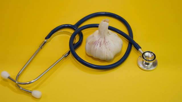 Une gousse d'ail avec un st&eacute;thoscope sur un arri&egrave;re plan jaune.