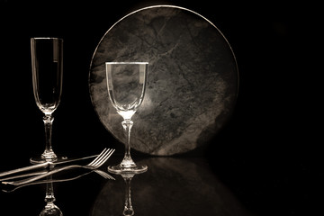 Verres à pied et assiette sur fond noir avec reflet.