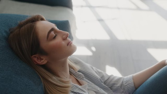 Serene attractive young woman resting on couch taking deep breath of fresh air, healthy calm lady relaxing on comfortable sofa napping feel stress free at home lounge alone sunny day sunlights