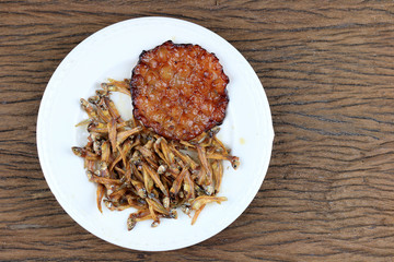 Fried giant catfish and pile of Deep fried small fishes (Minnow fish) Traditional Thai recipes in white dish on rustic wood background.  popular in Thailand, important export product of Thailand.