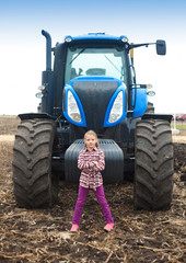 Cute girl near the modern tractor in the field.