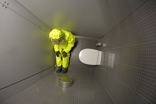 Quarantine - overhead view of man in protective coverall sitting  in the toilet and waiting.