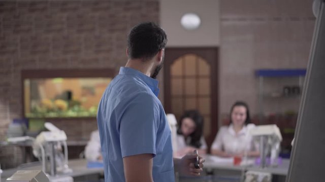 Close-up of confident Middle Eastern lecturer gesturing and talking to Caucasian students in dental audience. Portrait of male teacher giving lecture. Medicine, lifestyle, odontology, education.