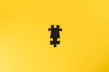 Two connected black puzzle pieces on a yellow background. The pieces in the centre of the frame