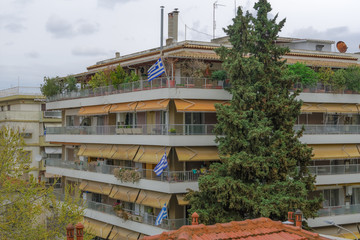 Fototapeta premium Greek flags waving on balconies for a national celebration. Blue and white Greek flags with cross outside city homes, celebrating the March 25 1821 day of Greek War of Independence.