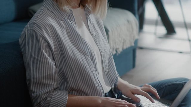 Beautiful woman sits on floor near the couch use laptop texting typing working study watch on-line vebinar or lecture business technology application slow motion close up