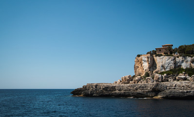 Blick auf felsige zerklüftete Landzunge Landspitze und Meer mit Wohnhaus auf Anhöhe unter blauem Himmel