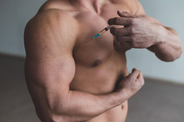 Close-up of a male torso. Unrecognizable shirtless bodybuilder man puts himself an injection of...