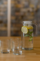 A jug of lemonade with a sprig of mint stands on a wooden table next to the glasses.