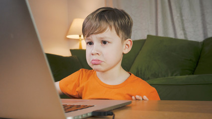 Sad boy using a computer. He feels disappointed studying at home. Home education concept. 