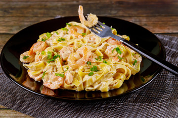 Alfredo fettuccine pasta with shrimps on black plate.